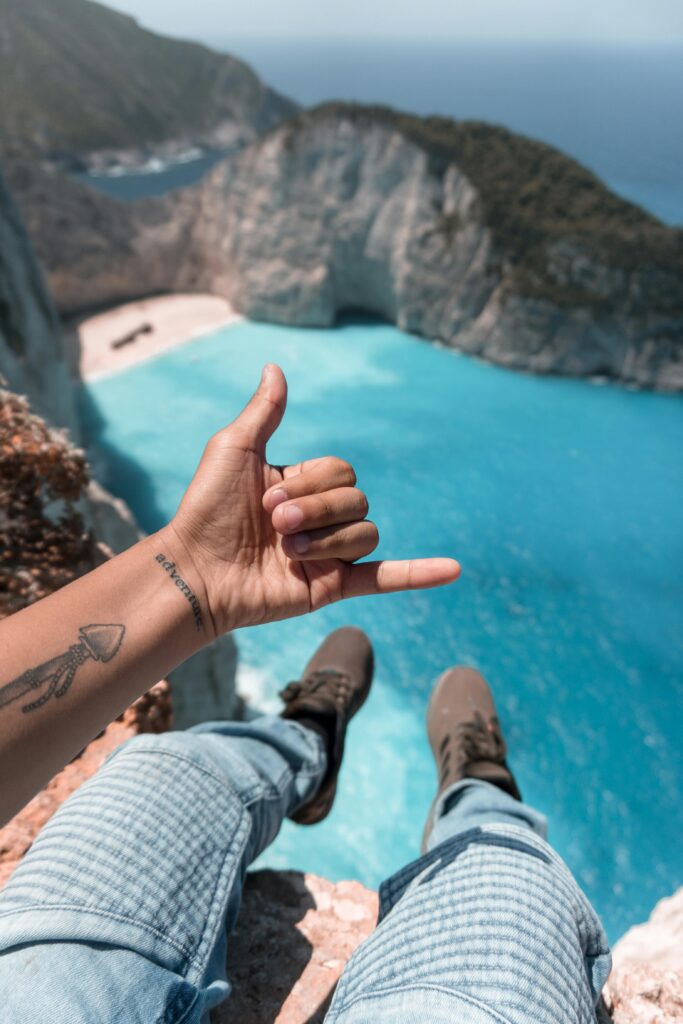 Person with tattoo gives hand gesture overlooking Zakinthos cliffs and sea.